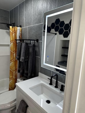Un baño moderno con lavamanos blanco, grifo negro y un espejo grande con azulejos hexagonales.