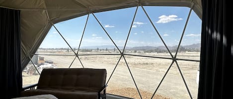 A tented room with a bed, a sofa, and a view of a dry landscape.