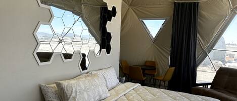 A tent-style room with a bed, a table, and chairs, and a view through a window.