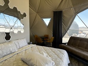 A tented room with a bed, a sofa, a table with chairs, and a view of the landscape.