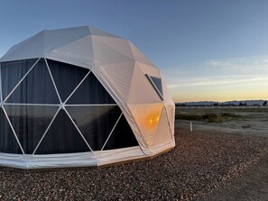 A geodesic dome structure with a black interior, set on a gravel surface with a clear sky in the background.