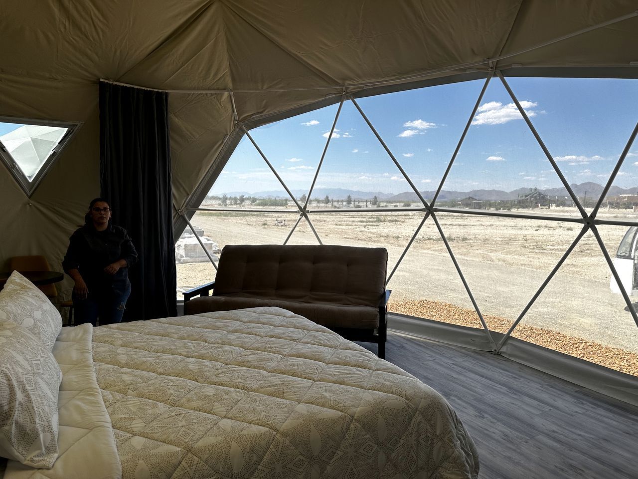 A tented room with a bed, a bench, and a view of a desert landscape.