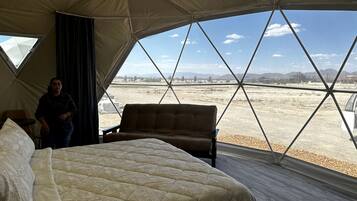 A tented room with a bed, a bench, and a view of a desert landscape.