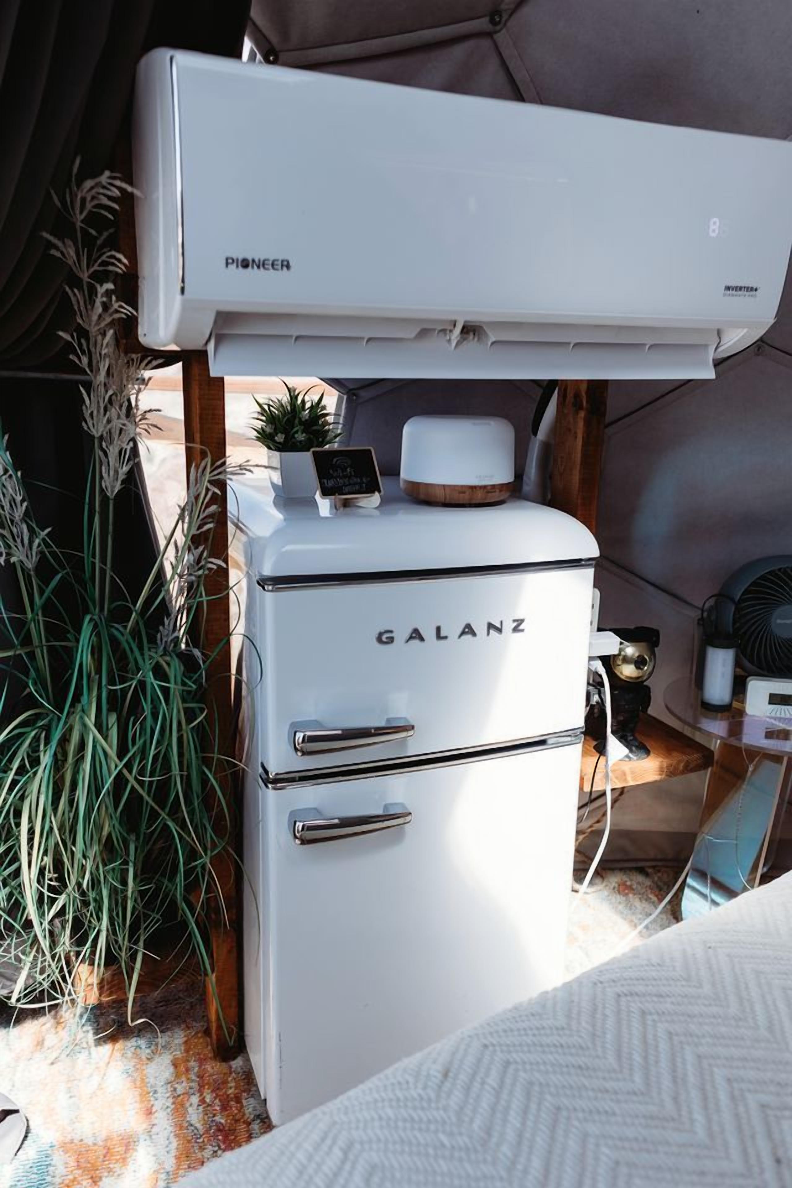 Un refrigerador blanco con la marca 'GALANZ' y un aire acondicionado 'PIONEER' encima.