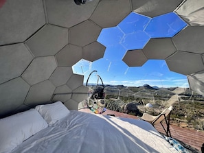 A hexagonal room with a bed, a hammock, and a view of a desert landscape.