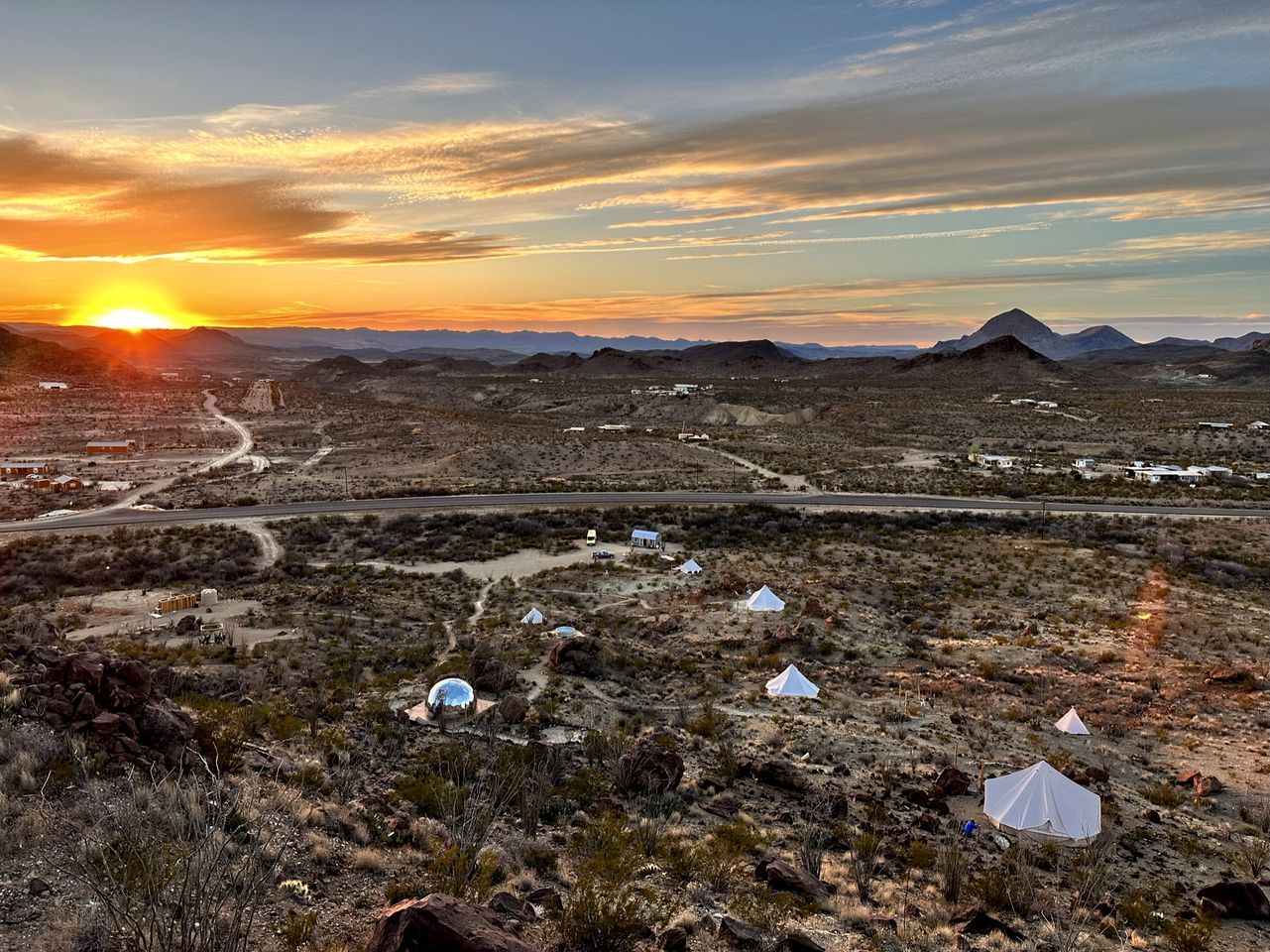 Paisaje desértico con tiendas de campaña y una carretera al atardecer.