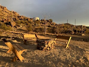 A sandy outdoor area with wooden benches and a stone fire pit. - Impressive Dome with Great Panoramic Desert Views in Terlingua, Texas (Terlingua)