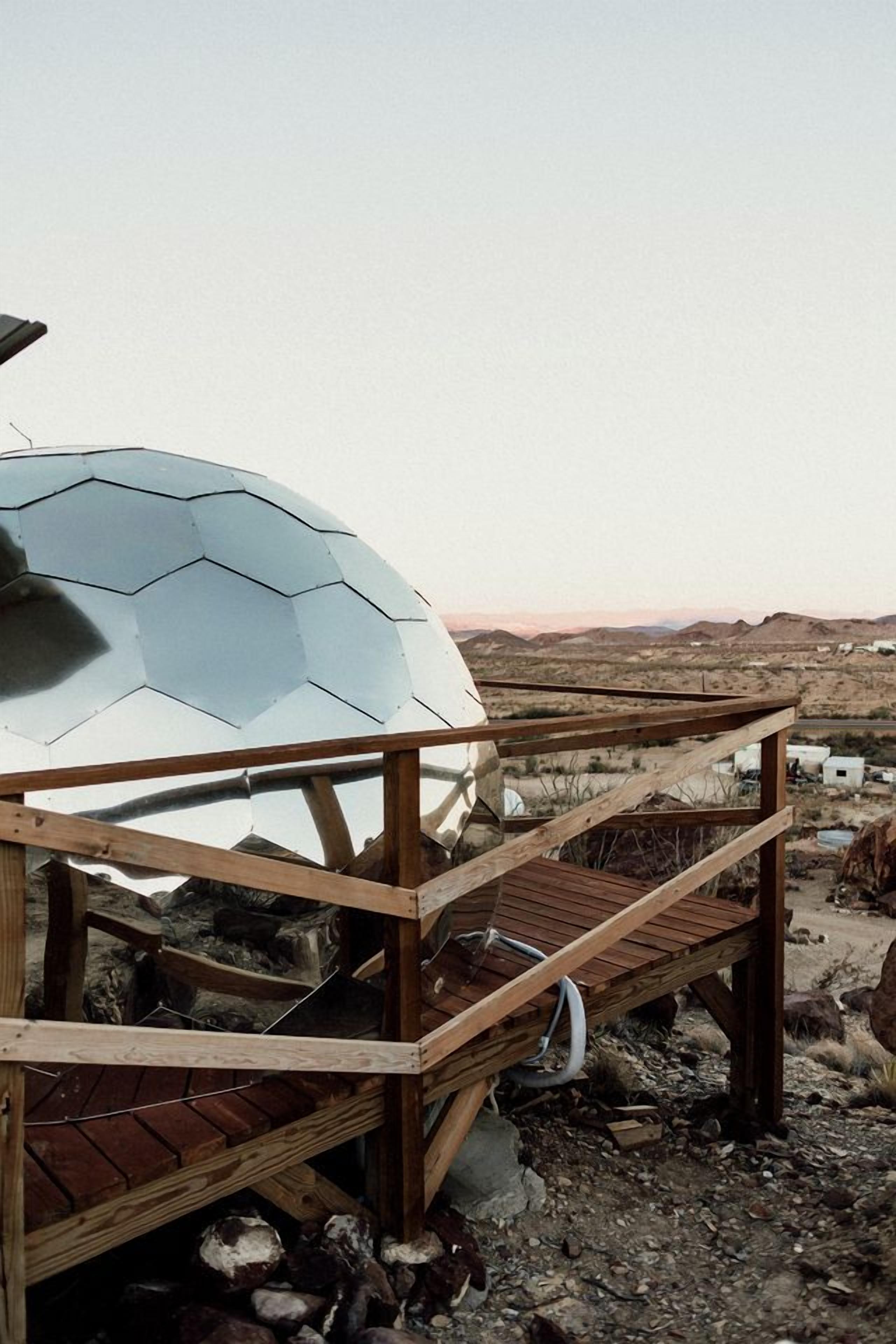 Una estructura de madera con un elemento en forma de cúpula, posiblemente una cúpula geodésica, y una terraza de madera.