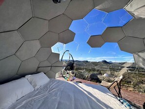 Ein sechseckiger Raum mit einem Bett, einer Hängematte und Blick auf eine Wüstenlandschaft.