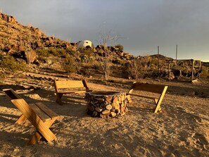A sandy outdoor area with wooden benches and a stone fire pit. - Impressive Dome with Great Panoramic Desert Views in Terlingua, Texas (Terlingua)
