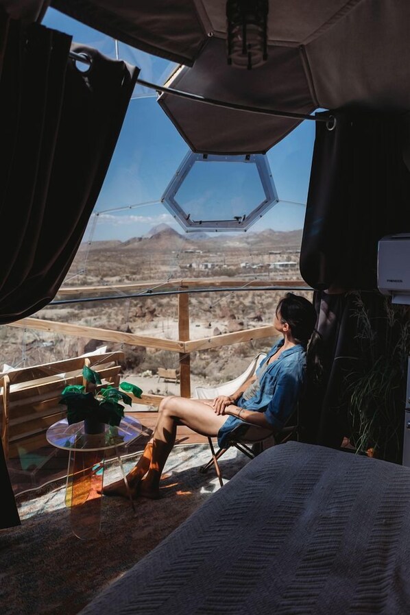 A person sitting on a chair in a tent-like structure with a view of a desert landscape.