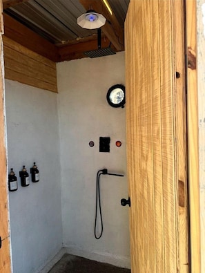 A small, enclosed shower area with a wooden door, a ceiling fan, and a wall-mounted heater.
