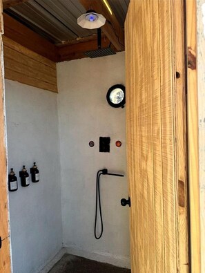 Ein kleiner, abgeschlossener Duschbereich mit Holztür, Deckenventilator und Wandheizung.