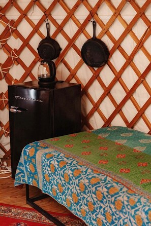 A room with a bed, a chest of drawers, and a wall-mounted rack with pots.