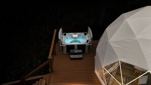 A hot tub on a wooden deck with a white dome structure nearby.