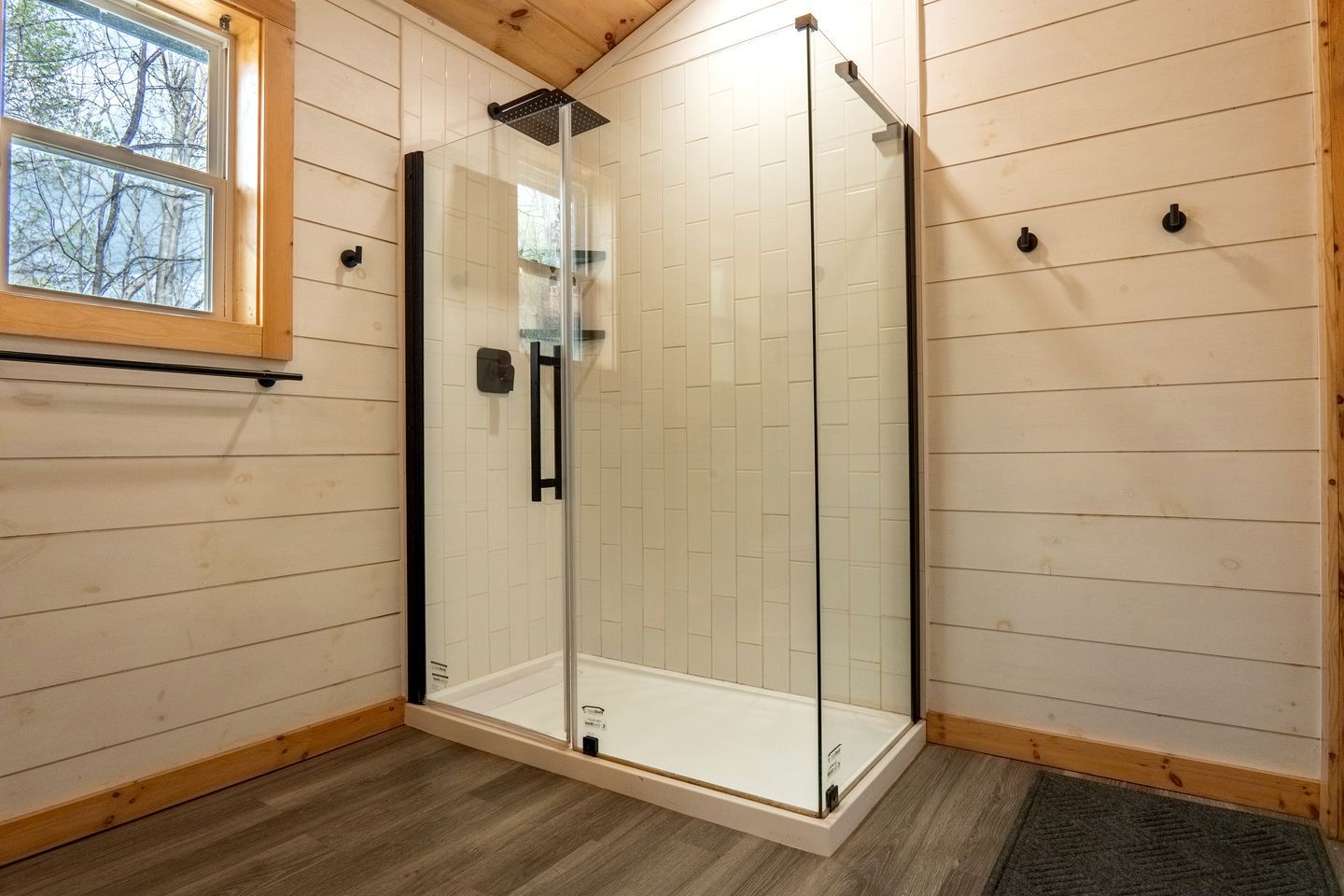 A glass-enclosed shower with a wooden floor and a window.