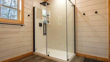 A glass-enclosed shower with a wooden floor and a window.