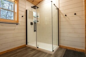 A glass-enclosed shower with a wooden floor and a window.