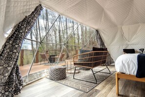 A tented accommodation with a bed, seating area, and a view of the forest.