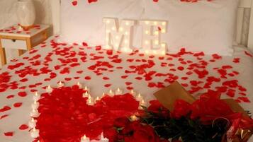 A bed with 'MARRY ME' illuminated letters, red rose petals, and a bouquet of roses.