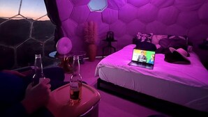 Ein Zimmer mit sechseckiger Decke, einem Bett mit Laptop und einer Flasche auf einem Tisch.