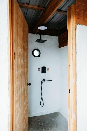 A small, enclosed space with a wooden door, a circular light fixture, a black switch, and a black hose. - Charming Cozy Dome in Terlingua, Texas (Terlingua)