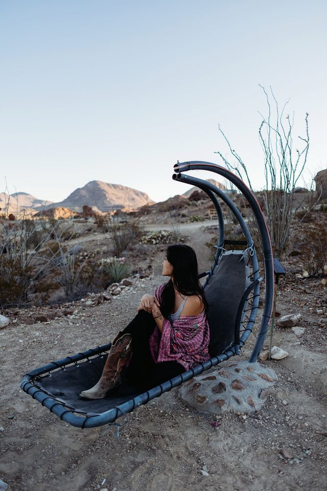 A person sitting on a hammock chair outdoors with a desert landscape in the background.