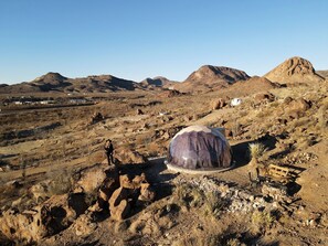 Paisagem desértica com uma grande estrutura em cúpula geodésica, terreno pedregoso e montanhas ao longe.