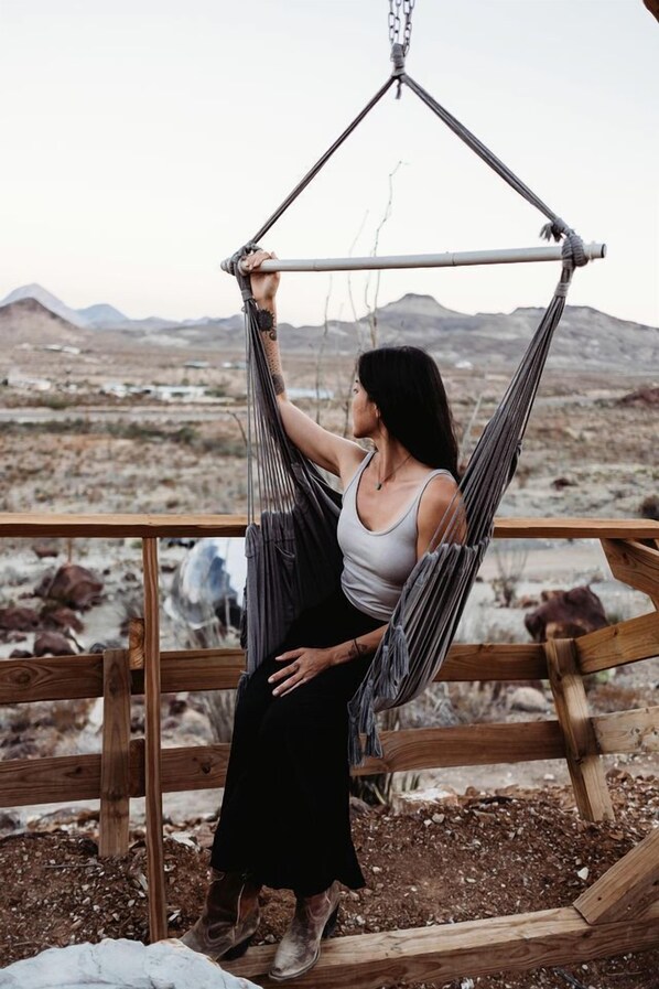 A person in a hammock with a view of a barren landscape and mountains.