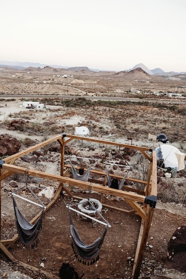 A wooden structure with hammocks and a white tent in a desert landscape.