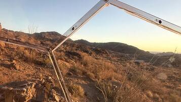 A geometric metal structure in a dry, rocky landscape with distant hills.