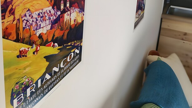 A poster of a mountainous landscape with a village, a green cushion, and a wooden floor. - Quiet, Ideally Located Apartment – Cozy and Newly Renovated (Briançon)
