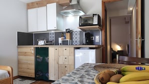 A compact kitchen with a microwave, toaster, and a small refrigerator. There is a dining table with a patterned tablecloth and a basket of fruit. - Quiet, Ideally Located Apartment – Cozy and Newly Renovated (Briançon)