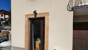 A building entrance with a wooden door, a small table, and a chair outside. - Quiet, Ideally Located Apartment – Cozy and Newly Renovated (Briançon)