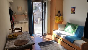 A cozy living room with a sofa, a dining table with a mat, a chair, a window with curtains, and a view of the outside. - Quiet, Ideally Located Apartment – Cozy and Newly Renovated (Briançon)