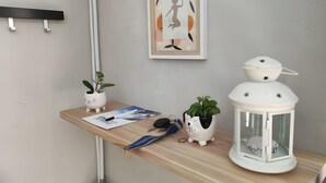 A room with a wooden shelf holding a framed artwork, two potted plants, a white lantern, and a magazine. - Quiet, Ideally Located Apartment – Cozy and Newly Renovated (Briançon)