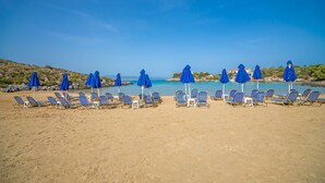 En strand med rader av blå parasoller och solstolar.