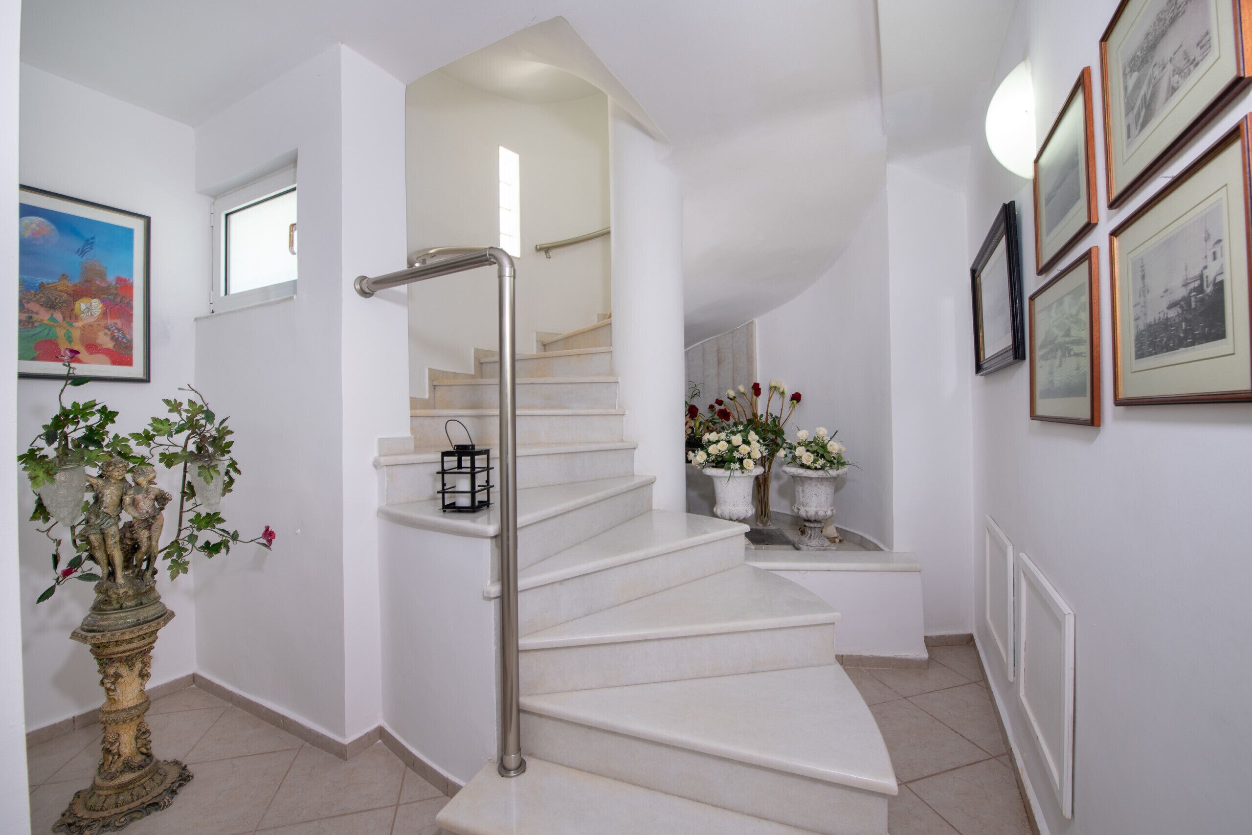 A staircase with a handrail, white walls, and framed pictures.