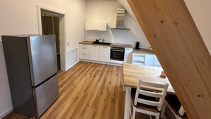 A modern kitchen with white cabinets, a wooden dining table, and a built-in oven. - Apartment 'Ferienwohnung Derday Im Schuttertal' with Balcony and Wi-Fi (Schuttertal)