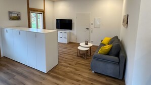 A modern interior with a wooden ceiling, a central island with a flat-screen TV, a grey sofa with yellow cushions, and a small round table. - Apartment 'Ferienwohnung Derday Im Schuttertal' with Balcony and Wi-Fi (Schuttertal)