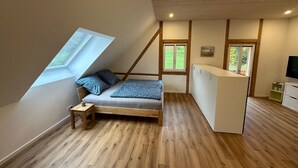 A loft bedroom with a slanted ceiling, a bed with pillows, a small table, a TV, and a window. - Apartment 'Ferienwohnung Derday Im Schuttertal' with Balcony and Wi-Fi (Schuttertal)