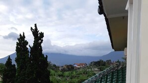 Un balcon avec deux chaises en plastique rouge, un sol carrelé et une vue sur une montagne et des maisons au loin.