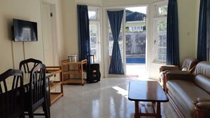 Un salon avec un canapé, une table basse, un téléviseur, une étagère en bois et une valise.