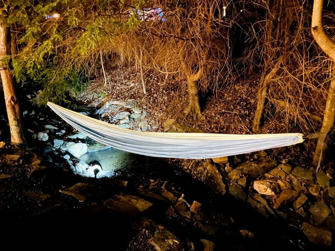 A hammock strung between trees over a rocky stream.