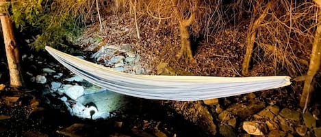 Una hamaca tensada entre árboles sobre un arroyo pedregoso.