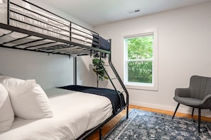 A bunk bed with a mattress and pillows, a chair, a window with a view of trees, and a patterned rug. - Peaceful Cottage with Hot-tub in Todd, North Carolina (Fleetwood)