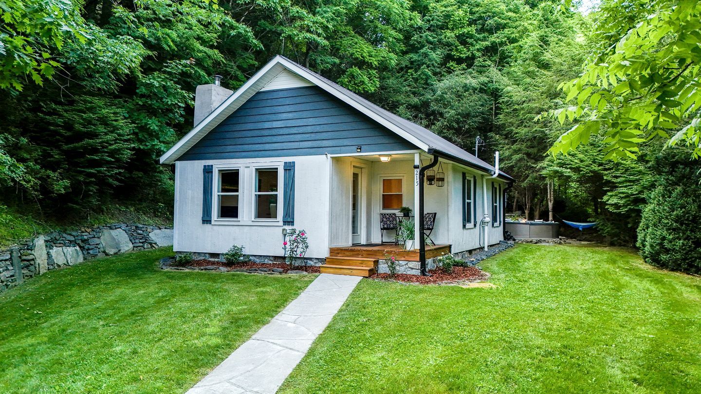 A small, single-story house with a sloped roof, a front porch, and a stone wall foundation.