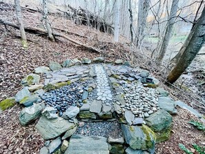 A circular stone structure surrounded by rocks and trees.