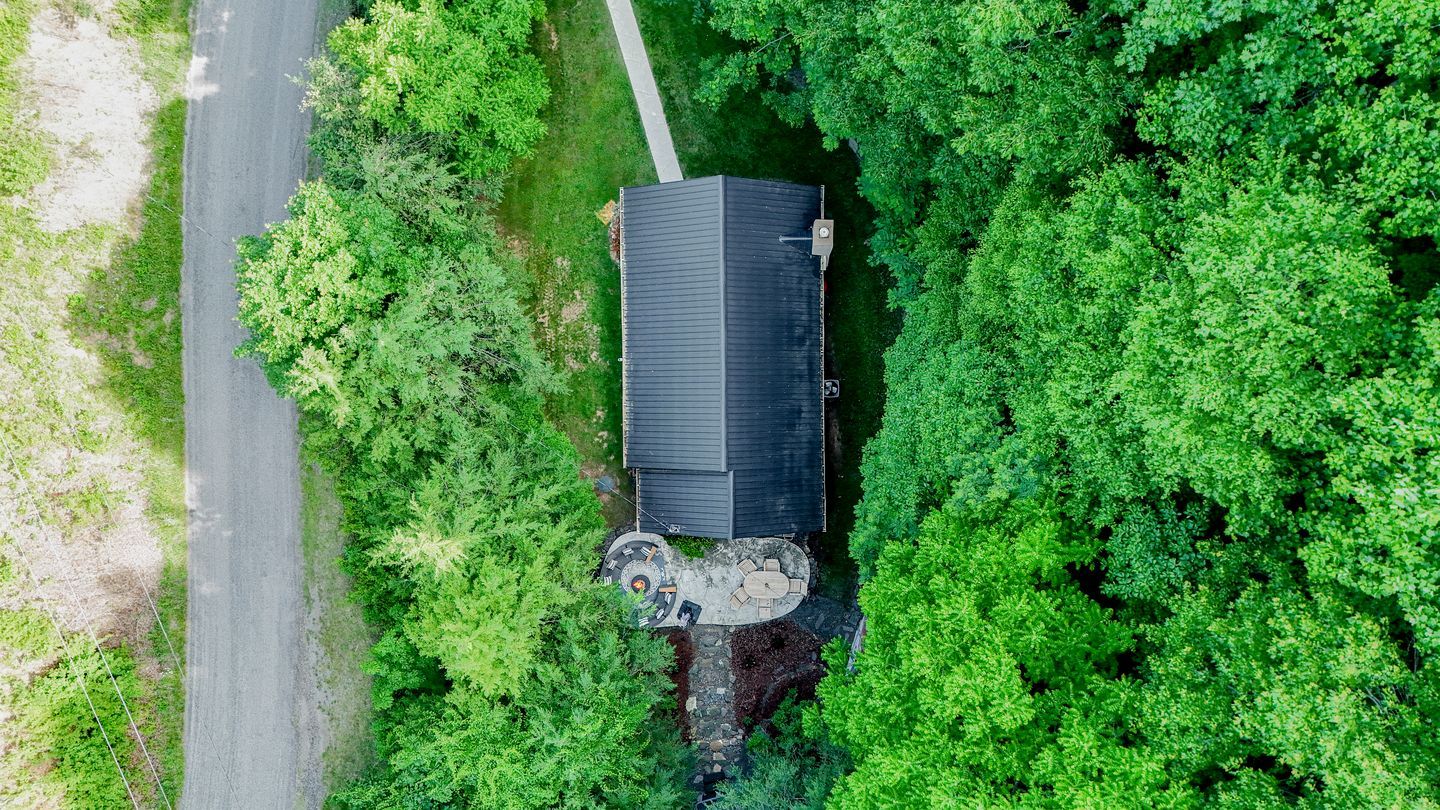 Une maison entourée d’un feuillage verdoyant et dense, avec une allée pavée et un patio aménagé avec du mobilier d’extérieur.