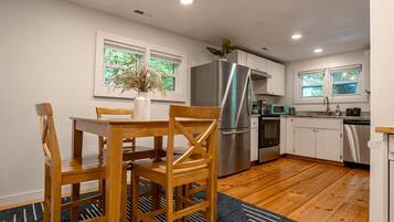 A modern kitchen with a dining area, featuring a stainless steel refrigerator, a microwave, and wooden flooring.